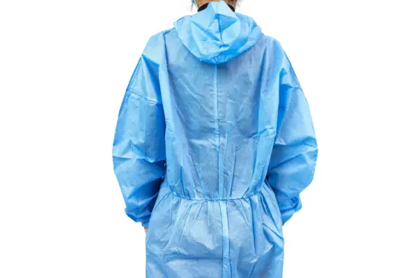 Blue hooded disposable coverall viewed from behind Person seen from behind wearing a blue hooded disposable coverall with elastic cuffs and waist against a white background.