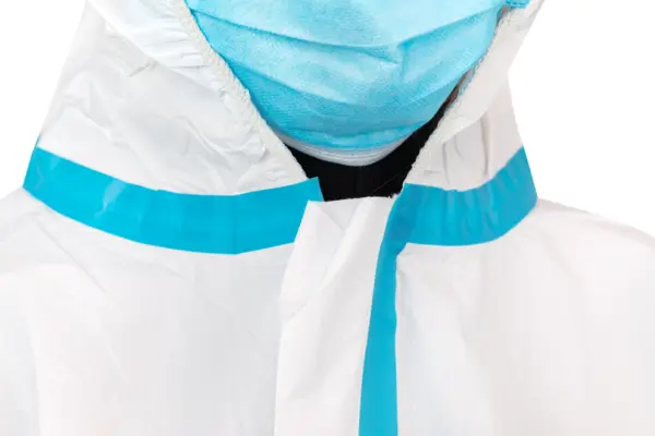 Close-up of worker wearing medical protective gear Close-up view of a person in a blue surgical mask and white protective coveralls against a plain background.