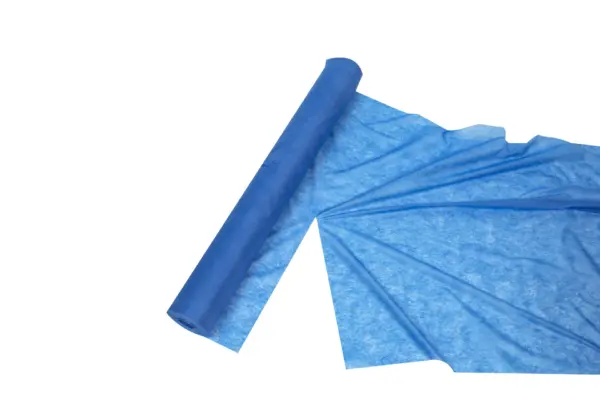 Blue nonwoven fabric roll partially unrolled across a white background, showing its thin textured material and wide sheet.
