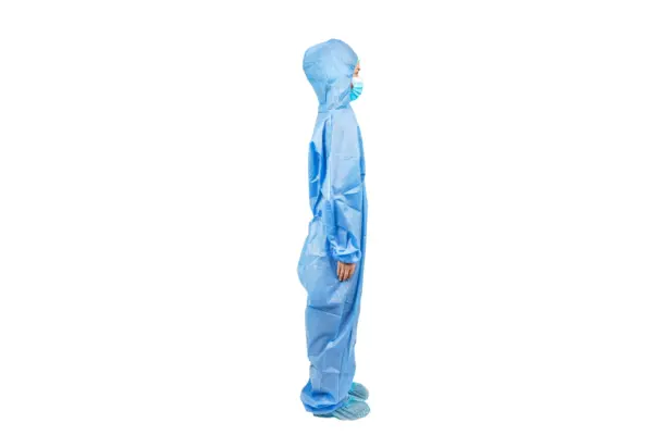 Blue protective coverall shown in side profile Person wearing a blue hooded protective coverall, face mask, and shoe covers while standing in side profile