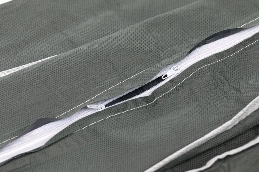 Close-up of a partially open white zipper sewn into textured dark green mesh fabric with contrasting white stitching.