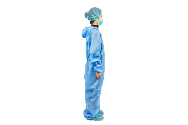 Medical worker wearing blue protective coveralls Healthcare worker in blue protective coveralls, hair cover, face mask, and shoe covers stands in profile against white