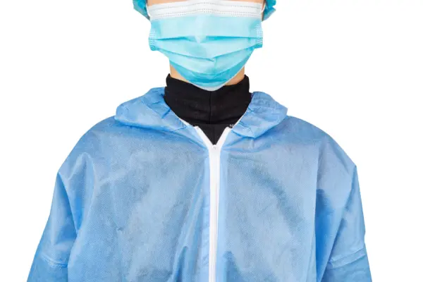 Person wearing a blue protective gown and face mask Close-up of a person wearing a blue disposable protective gown, surgical face mask, hair cover, and black turtleneck.