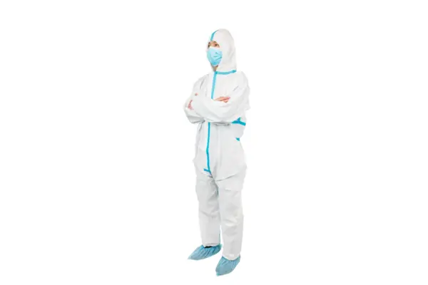 Worker in protective suit and face mask Person standing with folded arms in a white protective coverall, blue surgical mask, and blue shoe covers.