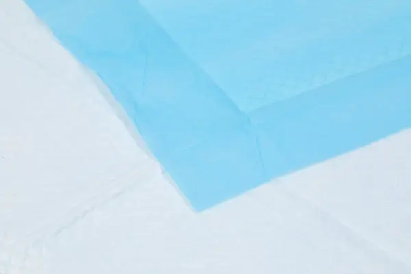 Close-up of a translucent blue sheet layered diagonally across a pale white surface with soft wrinkles and texture.