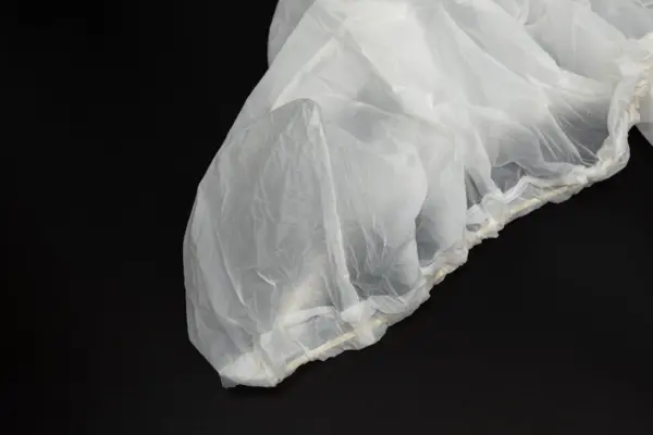Translucent protective cover on a black surface Crinkled translucent disposable plastic cover with a gathered elastic edge resting on a black background