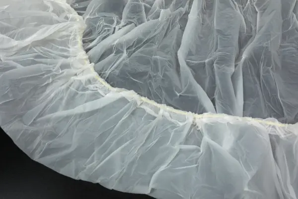 Translucent plastic sheet with elastic edge Close-up of a crumpled translucent white plastic sheet spread across a dark surface, with a gathered elastic edge.