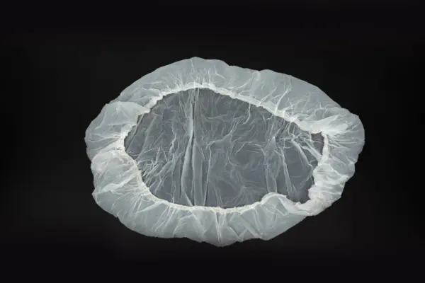 Transparent disposable shower cap on black background Transparent disposable plastic shower cap with an elastic gathered edge, laid flat against a plain black background.