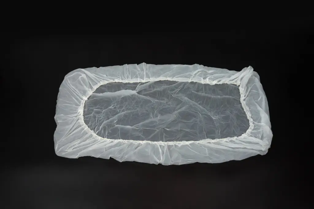 Translucent rectangular plastic cover with gathered elastic edging laid flat against a black background.