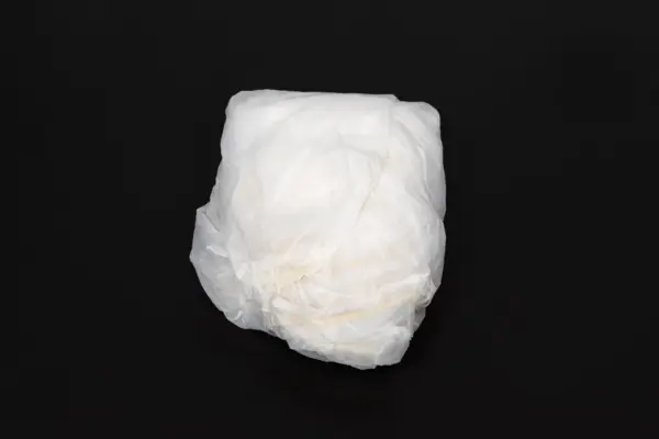 White disposable diaper on a black background Crumpled white disposable diaper shown from the outside, centered against a plain black background.
