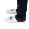 White house slippers worn with dark trousers White slip-on house slippers with dark trim worn on feet beneath dark trousers against a plain white background