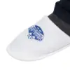 White mesh slip-on shoe with dark trim White mesh slip-on shoe with a rounded toe, blue printed emblem, and dark trim worn beneath dark trousers.