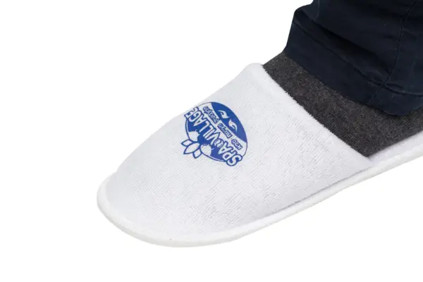 White mesh slip-on shoe with dark trim White mesh slip-on shoe with a rounded toe, blue printed emblem, and dark trim worn beneath dark trousers.