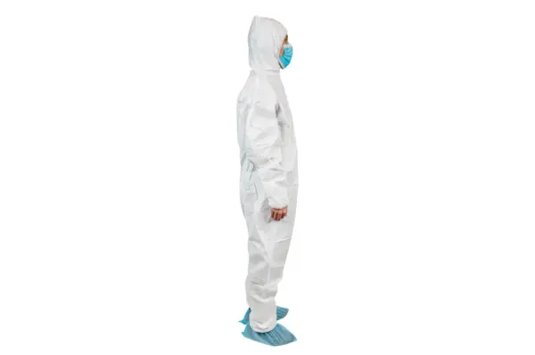 White protective coverall with mask and shoe covers Person in a white hooded protective coverall wears a blue surgical mask and disposable shoe covers against a white background.