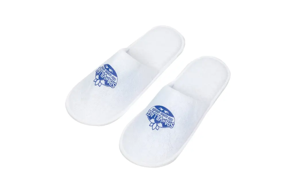 Pair of white open-back fabric spa slippers displayed on a plain white background, each featuring a blue printed logo.