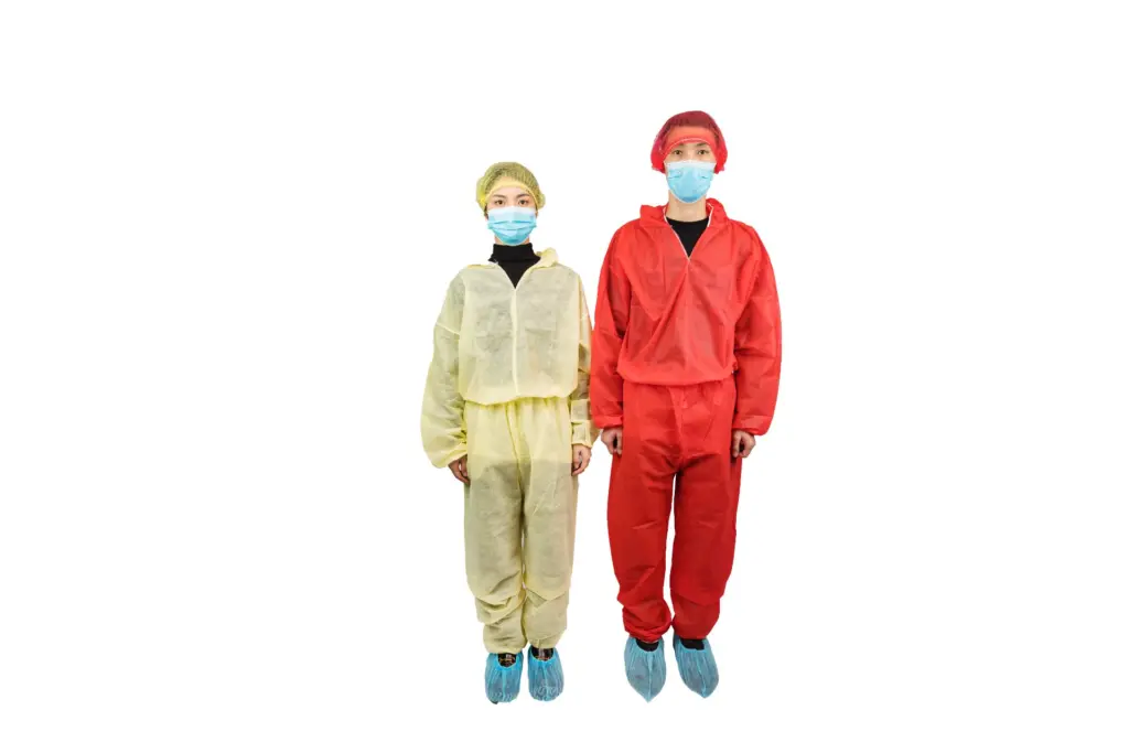 Two workers stand side by side wearing colored protective coveralls, hair covers, face masks, and blue shoe covers