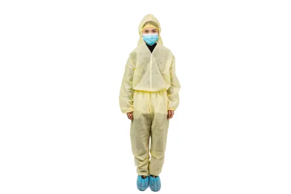 Person wearing protective coveralls and mask Person in yellow protective coveralls, hair cap, blue face mask, and shoe covers stands against a white background.